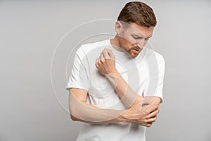 Unwell man holding aching elbow sore inflamed bones articulations. Studio isolated on background photo