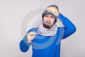 Unwell sick bearded man have temperature, holding thermometer an