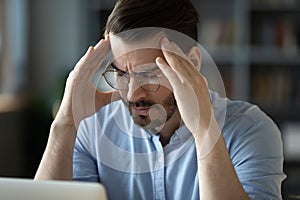 Unwell young man suffering from headache at workplace