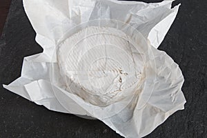 Unwrapped English Brie soft cheese on a grey slate background
