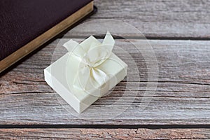 Unwrapped gift box with a ribbon and closed Holy Bible Book on a wooden background with copy space