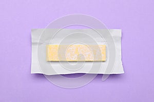 Unwrapped stick of chewing gum on violet background, top view