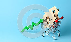 Up arrow and houses in shopping cart on blue background. Market growth in real estate prices