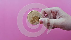 up close a hand holding golden Bitcoin over pink background