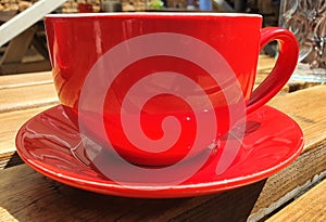 Up close red cup and saucer on a wooden bench in the sun.