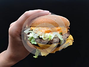 Up close a special beef burger in hand over black background with selective focus.