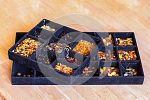 Up close view on a black tray for handcrafting with multiple sections filled with various kinds of amber and tools for crafting