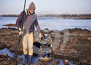 Up we go...a father and son walking on the rocks while out fishing together by the sea.