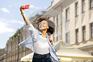 Upbeat curly woman taking selfies in the streets