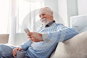 Upbeat elderly man texting while drinking coffee