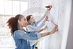 Upbeat female friends hanging a picture together
