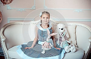 Upbeat girl and big white dog toy sitting on sofa inroom, decorated for she birthday party and holding