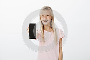 Upbeat girl showing new mobile phone to friends. Happy cute child with blond hair, pulling hand with smartphone