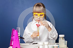 Upbeat schoolgirl in safety goggles watching chemical reaction going on in the flask. Huge interest. Science concept