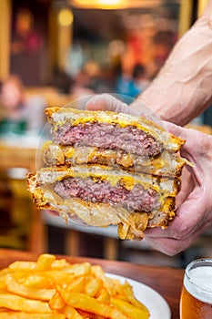 Upclose shot of hands holding a juicy meaty patty melt burger with cheese and grilled onions oozing out of it