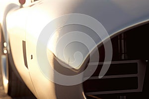 An upclose shot of a vintage racecar with chrome highlights and a bright white paint job the sun glinting off its Speed