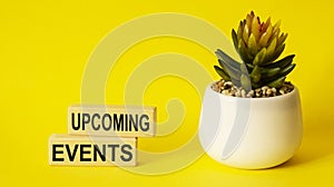 Upcoming events the word is made of building blocks next to a potted flower