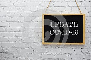 Update Covid-19 typography text on wooden blackboard hanging on white brick wall background