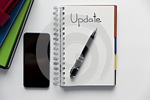 Update - handwritten text in a notebook on a desk. Project update checklist. Notebook, pen and books