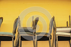 Upholstered chairs stacked against a bright yellow concrete block wall