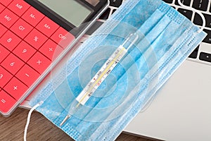 Upper face mask, mercury thermometer and calculator on laptop keyboard