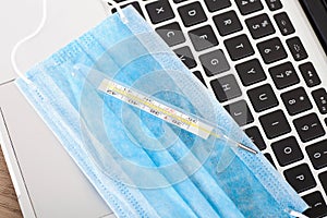 Upper face mask and mercury thermometer on laptop keyboard