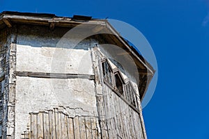 The upper part of an ancient watchtower made of stone blocks and wood paneling with windows against the blue sky on a bright sunny