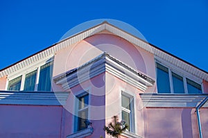 Upper part of facade of two-story house of pink color with sloping roof against the blue sky