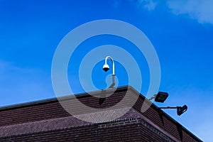 Upper part grunge vintage brick building one video security camera two floodlights mounted metal border sunny sky