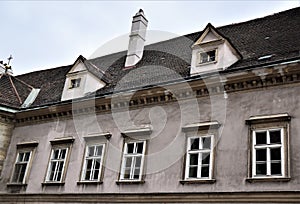 Upper part of a historic building in Vienna, simple but also elegant with six white windows and two dormers on the roof.