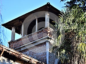 Upper part, immersed in the blue sky, of a tower with small columns and a palm tree in Padua.