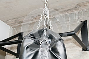 Upper part ob black punching boxing bag with chains closeup.