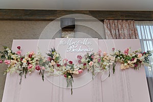 Upper part of pink decorative wedding arch, screen with flowers, just married names. Presidium with Mr. and Mrs. inscription.