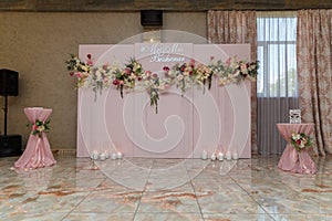 Upper part of pink decorative wedding arch, screen with flowers, just married names. Presidium with Mr. and Mrs. inscription.