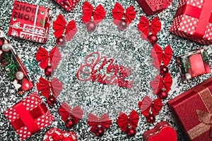 Upper, top, view from above of an Merry Christmas inscription inside of a circle created from red bows and evergreen toys surround