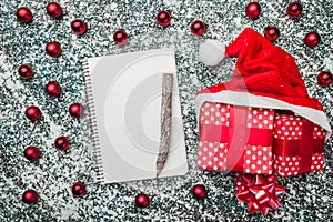 Upper, top, view from above of a notepad, wooden vintage pen, evergreen red toys, Christmas presents and Santa hat