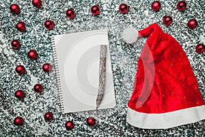 Upper, top, view from above of a notepad, wooden vintage pen, evergreen red toys, Santa hat on gray marble background