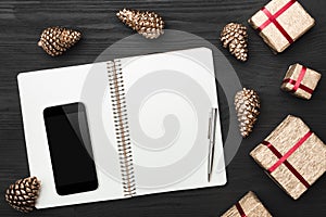 Upper, top view, of Christmas presents on a wooden black rustic background, note pad, pen, phone with space.