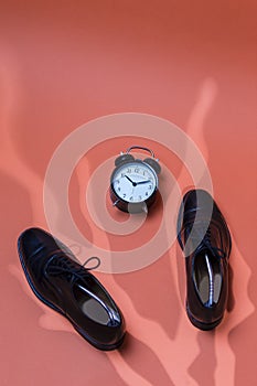 Upper View of Pair of Formal Male Stylish Black Polished Oxford Leather Laced Shoes Placed Together With Watch Clock Over Orange