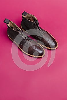 Upper View of Pair of Premium Dark Brown Grain Brogue Derby Boots Made of Calf Leather with Rubber Sole Placed On Pink Background