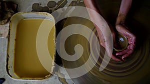 Upper view woman makes small pot with yellow clay on wheel
