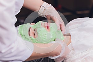 Upper view of a womansUpper view of a woman`s face covered by alginate mask while leaning on a spa bed.