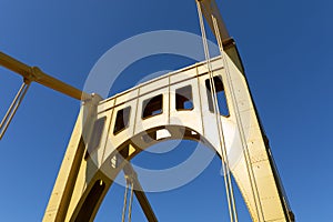 Upright of a self anchored suspension bridge painted bright yellow against a deep blue sky