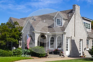 Upscale grey brick home with multiple gables and fireplace and landscaping and flowers and American Flags displayed