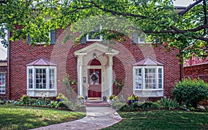 Upscale house with pillared porch and landscaping and bay windows with maple trees in front yard