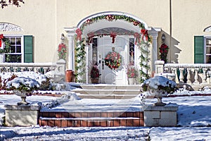 Upscale landscaped  stucco house with elegant entryway with columns decorated for Christmas with big wreath and garland on bright