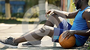 Upset African American basketball player sitting on ground, holding ball