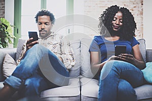 Upset african american couple relaxing together on the sofa.Young black man and his girlfriend using smartphones while