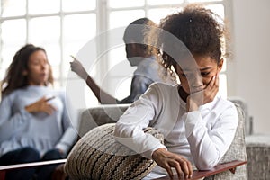 Upset African American girl sitting alone, parents quarreling