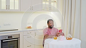 Upset african american man reading message on smartphone having tea.